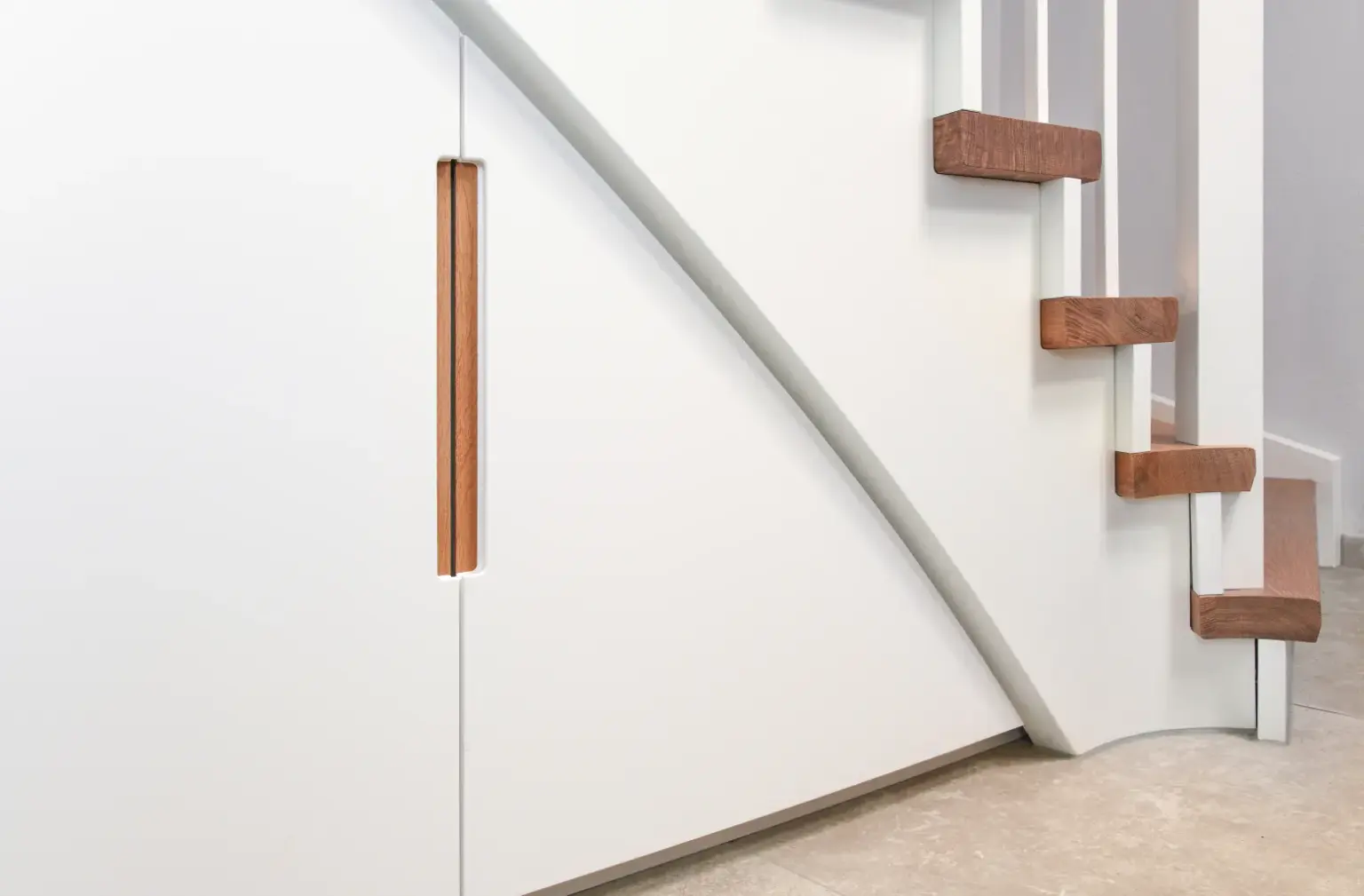 Nahaufnahme einer modernen weißen Treppe mit Holzstufen und einem eingebauten Stauschrank darunter, mit einem vertikalen Holzgriff und minimalistischem Design.