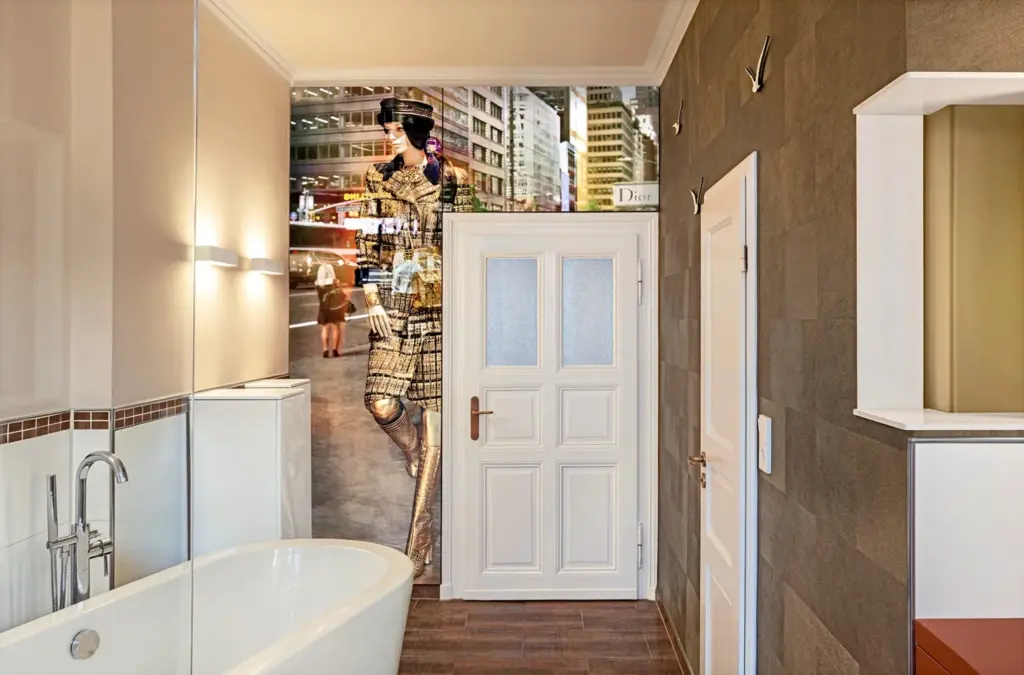 Modernes Badezimmer mit weißer Badewanne und beigen Wänden; eine Tür ist mit einer großen Fototapete versehen, die ein Fotomodell in einer städtischen Straßenszene zeigt und den urbanen Stil mit der Innenarchitektur verbindet.