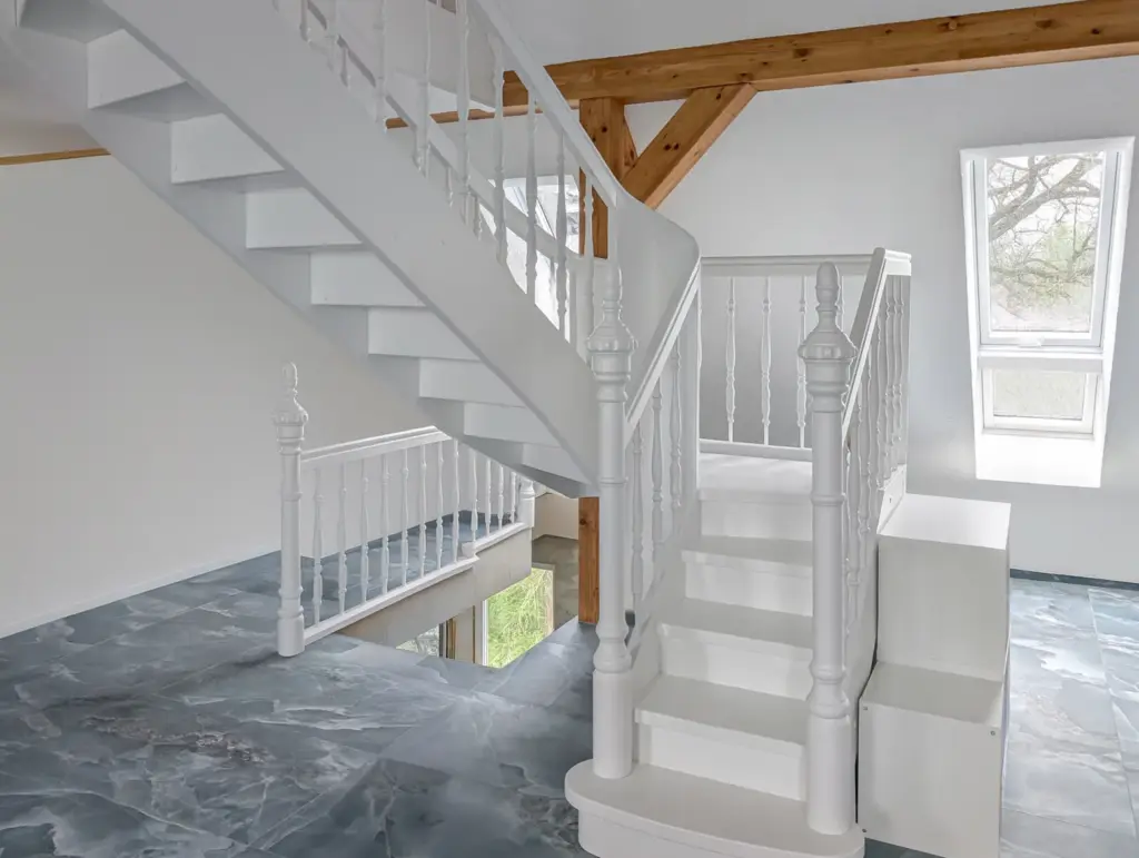 Ein modernes Interieur mit weißer Holztreppe, weißem Geländer, grauem Marmorboden, großen Fenstern und freiliegenden Holzbalken an der Decke.