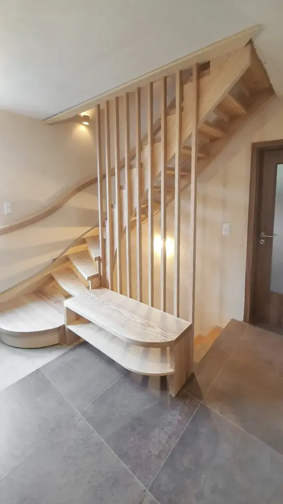 Eine moderne Holztreppe mit vertikalen Latten, geschwungenen Stufen und einer eingebauten Bank, die sich in einem hellen Raum mit gefliestem Boden und einer Holztür in der Nähe befindet.