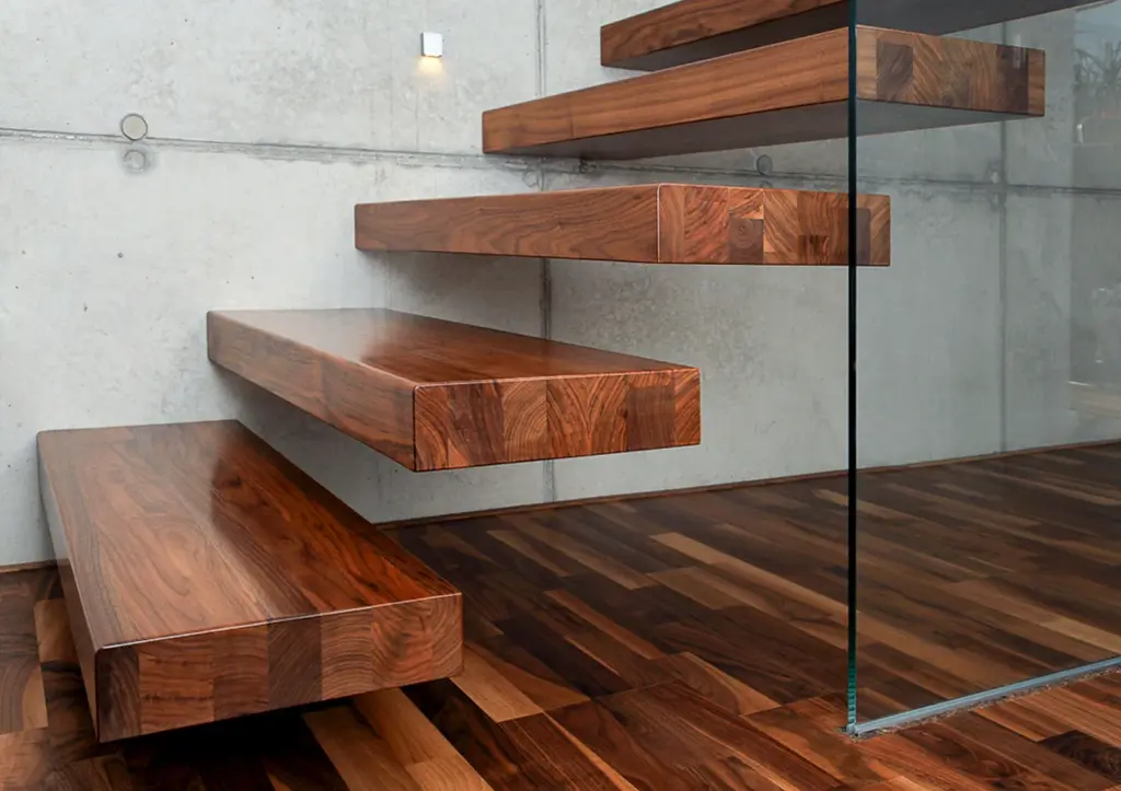 Schwebende Holztreppe mit dicken, rechteckigen Stufen an einer Betonwand, mit Glasgeländer und passendem Holzboden, alles in einem modernen, minimalistischen Innendesign.