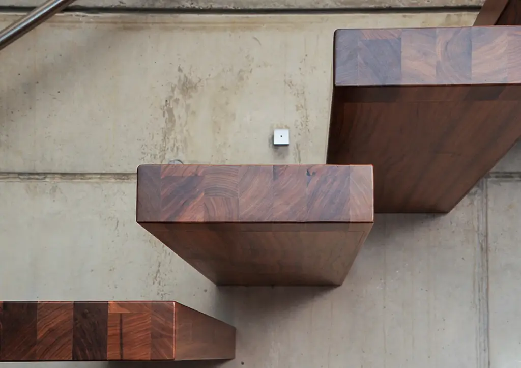 Nahaufnahme einer modernen Schwebetreppe mit dicken, rechteckigen Holzstufen, die an einer Betonwand befestigt sind, von oben gesehen.