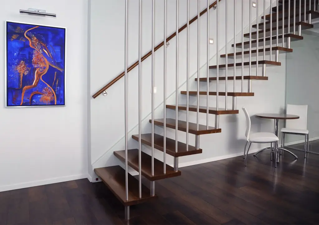 Modernes Interieur mit einer schwebenden Holztreppe, einem eleganten Metallgeländer, einem runden weißen Tisch mit zwei Stühlen, einem dunklen Holzboden und einem kräftigen blauen abstrakten Gemälde an der weißen Wand.