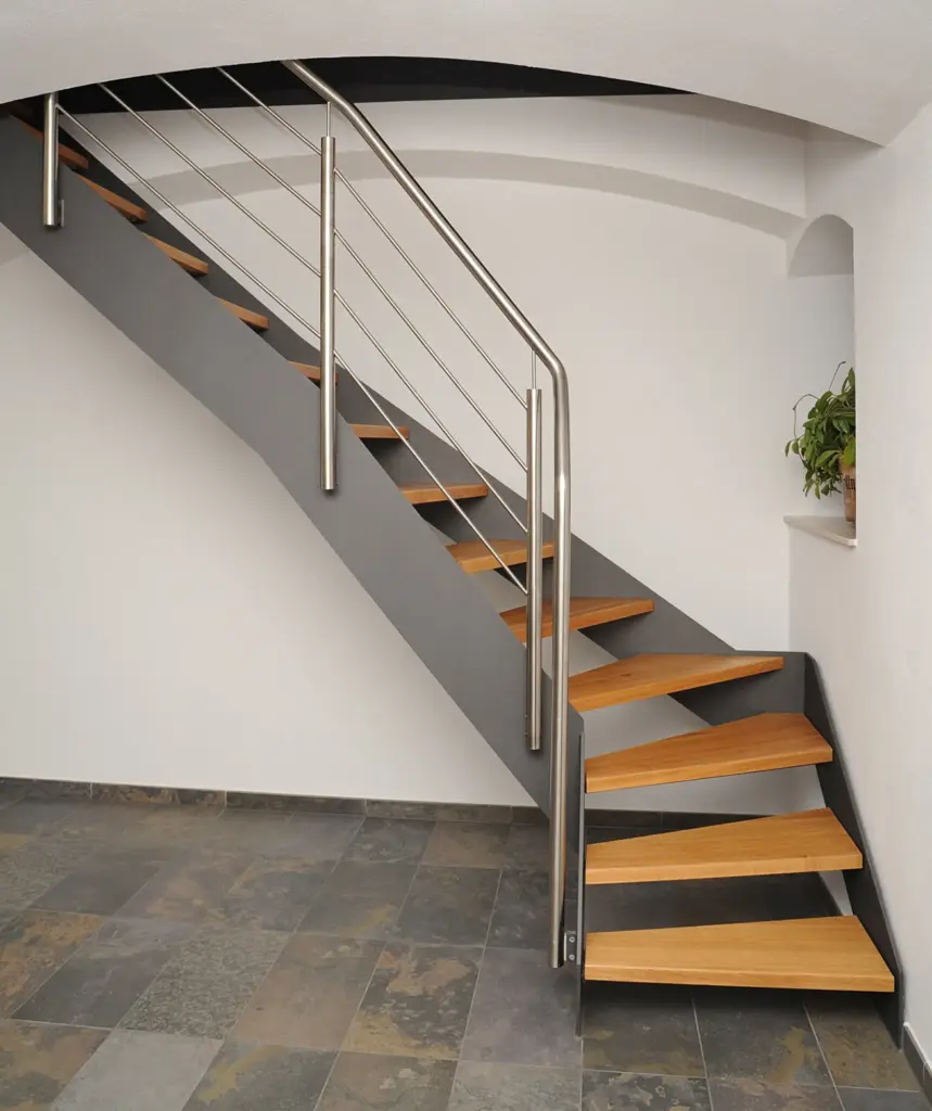 Moderne Treppe mit Holzstufen und einem eleganten Metallgeländer vor einer weißen Wand und einem grau gefliesten Boden. Eine kleine Pflanze steht rechts auf einem Fenstersims.